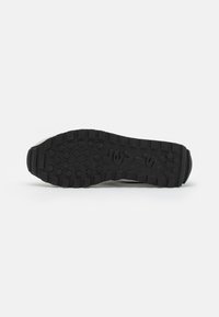 Schwarze Gummi-Außensohle eines Sneakers mit einem Profilmuster, das hexagonale und kreisförmige Griffe für besseren Halt bietet. Text Branding sichtbar.