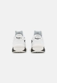 Vita och svarta atletiska skor med texturerad ovandel, dämpade sulor och en logodetalj på hälen. Bakre vy.