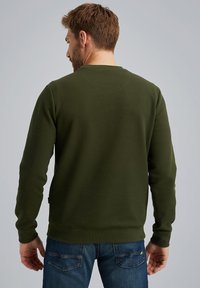 Sweatshirt vert olive avec un design texturé à côtes et un col rond. Poignets et ourlet ajustés, associé à un jean en denim bleu.