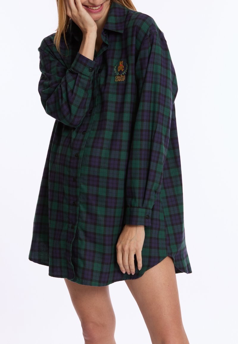 Groene en paarse geruite flanellen jurk met knoopjes aan de voorkant, lange mouwen en zijsplitten. Beschikt over een geborduurd rozenontwerp op de borst.
