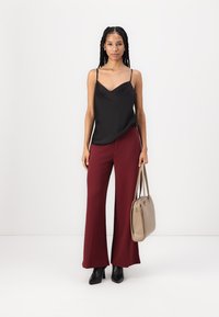 Zwarte satijnen camisole top met dunne bandjes, gecombineerd met hooggetailleerde bordeauxrode wijde broek. Draagt een beige handtas en zwarte hakken.