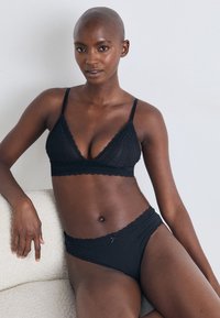 Black lace bralette and matching brief set. Soft, delicate fabric with scalloped edges. Minimalist design with a small bow accent on the brief.