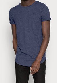 Mörkblå t-shirt med kort ärm gjord av mjukt, texturerat material med rund halsringning och en liten logotypdetalj på bröstet.