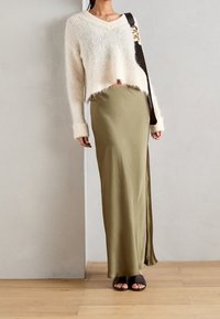 Pull en tricot blanc et fluffy avec un ourlet court et des manches longues, associé à une jupe maxi en satin vert olive ajustée et des sandales à glisser noires.