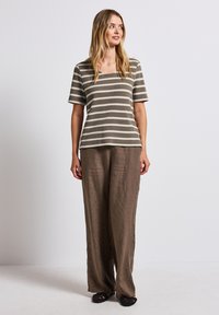 Lehký pruhovaný top v hnědé a krémové barvě se čtvercovým výstřihem, spárovaný s volnými hnědými lněnými kalhotami a černými otevřenými sandály.