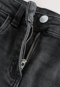 Schwarze Jeans aus Denim mit einem polierten Metallreißverschluss, feiner Textur und einem Bund mit Gürtelschlaufe und Knopfverschluss.