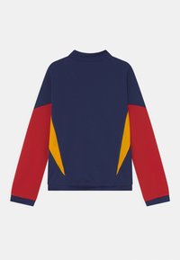 Marinjacka med röda och gula accentpaneler, långa ärmar och hög krage. Tillverkad av ett mjukt tyg med en åtsittande design.