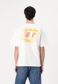 White cotton t-shirt features a graphic in yellow and pink on the back, with a relaxed fit and short sleeves. Casual, lightweight design.