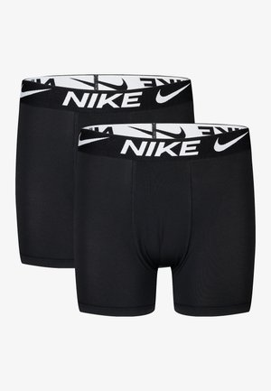 Dwie czarne bokserki Nike z białymi gumkami z logo, pokazane nałożone na siebie na jednolitym tle.