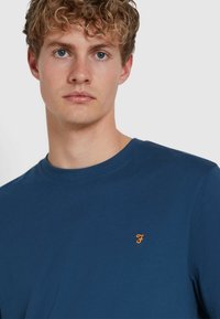 T-shirt di cotone blu navy con scollatura rotonda e maniche corte, con un piccolo logo ricamato arancione sul petto.
