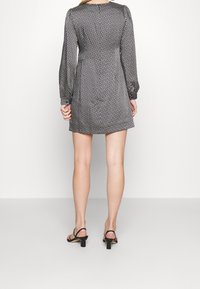 Černobíle potištěné šaty s dlouhými rukávy, kulatým výstřihem a volným střihem. Vzor obsahuje geometrické tvary; nošeny s černými sandály.