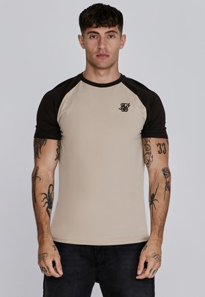 T-shirt aderente beige con maniche a raglan nere e un piccolo logo nero sul petto. Presenta una texture liscia e un collo rotondo.