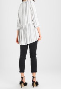 Hvid- og gråstribet tunika med trekvartærmer, samlet talje og længere bag. Sammen med sorte cropped jeans og hæle med pelsdetaljer.