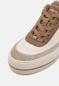 Sneaker met een bovenwerk van beige leer, bruine suède accenten en een gestructureerd bruine veter. Heeft een dikke witte zool en een metallic logo detail.