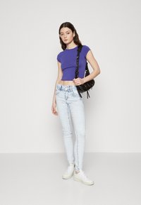 Ljubičasti uski crop top, svijetloplave skinny traperice sa izblijedjelim dijelovima, i bijele teniske cipele. Dodaci uključuju crnu torbicu preko tijela sa teksturom.