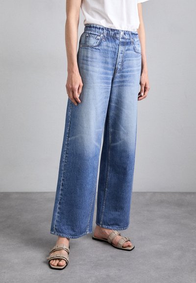 Jeans din denim de culoare albastră deschisă, cu picioare largi, având o croială relaxată, talie elastică și o ușoară decolorare în apropierea fundului. Asortate cu sandale ușoare.