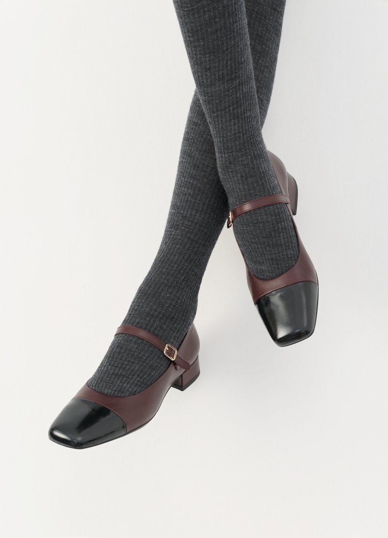 Burgundy läderskor med Mary Jane-design, med en svart lacktå och smal ankelrem; bärs med mörkgrå ribbade strumpor. Låg blockklack.