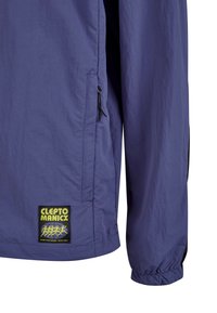Lila leichte Jacke mit einer Seitentasche, elastischen Bündchen und einem rechteckigen Logo-Patch mit dem Text "CLEPTO MANICX".
