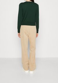 Zielony, długi sweter z okrągłym dekoltem, zestawiony z beżowymi, szerokimi spodniami z tylnymi kieszeniami i miękką fakturą.