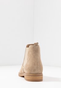 Stivaletti beige in camoscio con pannelli elastici ai lati e tacco basso a blocco, caratterizzati da una texture liscia e un colore uniforme.