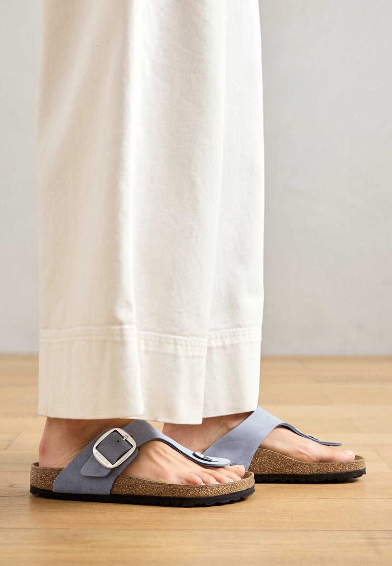 Blaue Wildleder-Flip-Flop-Sandalen mit einem Korkfußbett, ausgestattet mit einer großen silbernen Schnalle und einer schwarzen strukturierten Gummisohle.