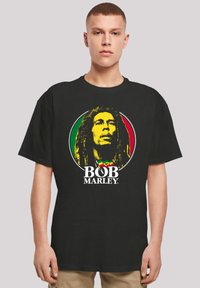 Black cotton t-shirt featuring a circular graphic of Bob Marley in yellow, surrounded by red and green, with "BOB MARLEY" printed below.