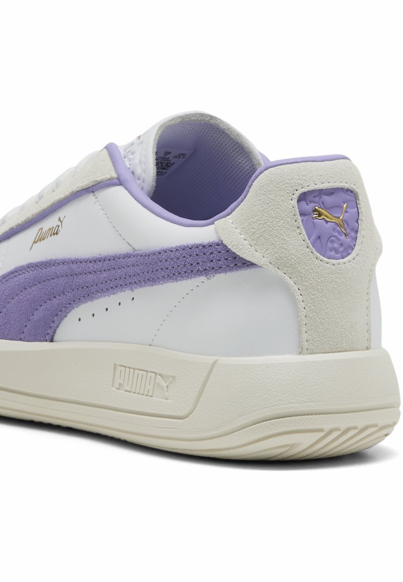Puma Sneaker mit einem Obermaterial aus weißem Leder und Lavendel-Suede-Akzenten, einer strukturierten Ferse und einer Gummisohle. Goldenes Logo-Detail an der Seite.