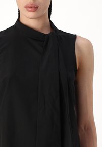 Haut sans manches noir avec un col haut et un drapé avant fluide. Tissu lisse et léger avec un minimum de détails et une coupe décontractée.