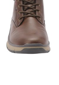 Hnedá kožená čižma s okrúhlym prstom, textúrovaným povrchom, hnedými šnúrkami a kontrastnou béžovou gumovou podrážkou s čiernym vzorom.