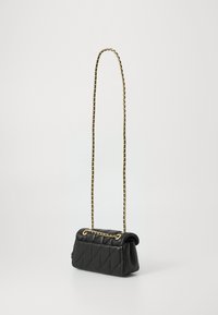 Sac à main en cuir matelassé noir avec une chaîne, doté d'un haut courbé, de quincaillerie dorée et d'une forme structurée, mesurant environ 25 cm.