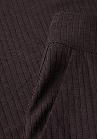 Donkerbruin geribbeld stof met verticale strepen, met een gladde textuur en een licht omgevouwen zoom. Zichtbare stiksels langs de randen.