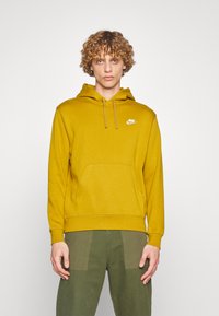 Sweatshirt mostarda com capuz e cordão, bolso canguru e logótipo branco da Nike no peito. Tecido suave com um corte descontraído e punhos canelados.