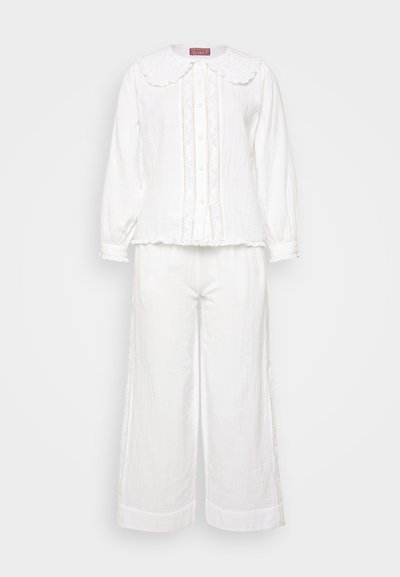 Bijeli dvodijelni outfit koji se sastoji od košulje s dugim rukavima i velikim valovitim ovratnikom, ukrašenim šavovima, u kombinaciji sa hlačama širokih nogavica.
