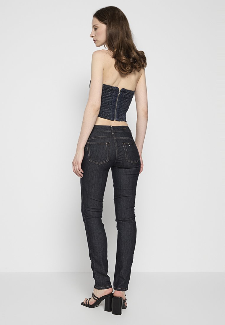 Jeans in denim scuro a vestibilità aderente, con una texture liscia, tasche posteriori e una leggera cucitura sui bordi. Top in stile corsetto di colore blu navy con chiusura a zip.