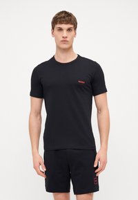 T-shirt en coton noir à manches courtes, col rond, avec un logo "HUGO" rouge sur la poitrine, associé à un short noir avec un détail de logo rouge.