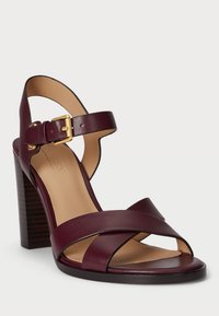 Burgundi bőr magassarkú szandál keresztpántos rögzítéssel, bokapántos csattal és fából készült talppal. Simább textúrájú, minimál dizájnnal.