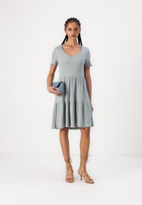 Vestido ribbed azul claro com decote em V, mangas curtas e saia em camadas. A bainha é desfiada, combinado com uma pequena bolsa azul e saltos com tiras.