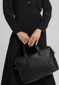 Schwarze Ledertasche mit zwei Griffen, rechteckiger Form, strukturierter Oberfläche und einer Vorderfach. Oben mit einem Reißverschluss verschlossen.