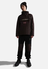 Dark brown waterproof jacket with a front pocket and Norwegian flag. Black fleece pants with brown panels. Black sneakers and beanie.