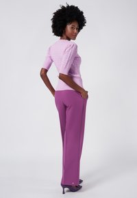 Lila stickad topp med korta puffärmar, tillsammans med högmidjade lila byxor och lila högklackade skor. Detaljerad textur synlig.