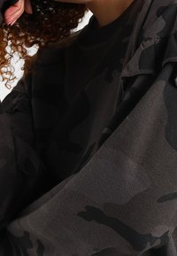 Svart kamouflage sweatshirt med samlade ärmdetaljer, tillverkad av mjukt bomullsmaterial, med rundad halsringning och strukturerat mönster.