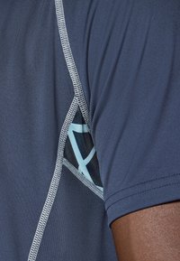 Jūras spēku sporta krekls ar sieta paneli un gaiši zilu ģeometrisku rakstu. Redzamās kontrastējošās šuves uzlabo dizainu. Mīksts, viegls audums.