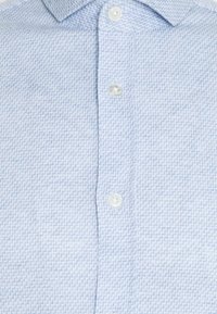 Camicia button-up azzurro chiaro con un motivo tessuto testurizzato. Presenta un colletto classico e bottoni bianchi lungo la patta.