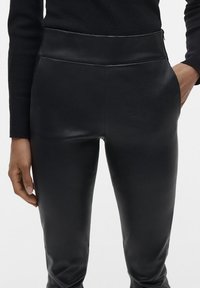 Zwarte high-waisted leren broeken met een gladde textuur en een slim fit, met een verborgen rits aan de zijkant voor sluiting.