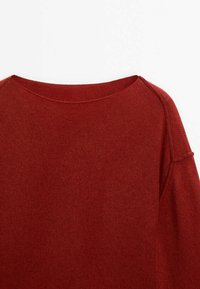 Pull en maille rouge avec un large décolleté, une texture côtelée et des coutures d'épaule tombantes. Le tissu semble doux et léger.