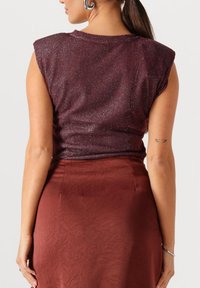 Donkerrode top met een sprankelende textuur en gewatteerde schouders, gecombineerd met een gladde, roestkleurige rok met een geplooid patroon.