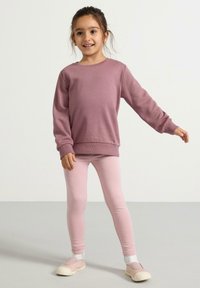 Violetti collegepaita pitkillä hihoilla, yhdistettynä vaaleanpunaisiin legginsseihin ja liukuoviin kenkiin. Sileä pinta, rento muotoilu, mukava istuvuus.