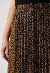 Leopardmönstrad plisserad kjol i brunt och svart tyg. Har en texturerad design och elastisk midja för komfort.