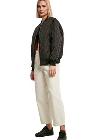 Schwarze gesteppte Bomberjacke mit gerippten Bündchen und Bund, kombiniert mit lockeren weißen Hosen und schwarzen Sneakers. Einfaches, strukturiertes Design.