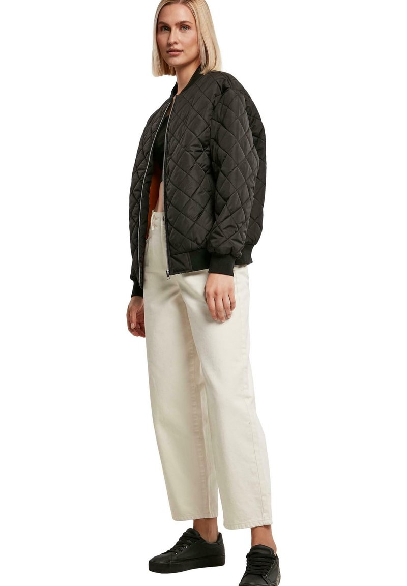 Schwarze gesteppte Bomberjacke mit gerippten Bündchen und Bund, kombiniert mit lockeren weißen Hosen und schwarzen Sneakers. Einfaches, strukturiertes Design.